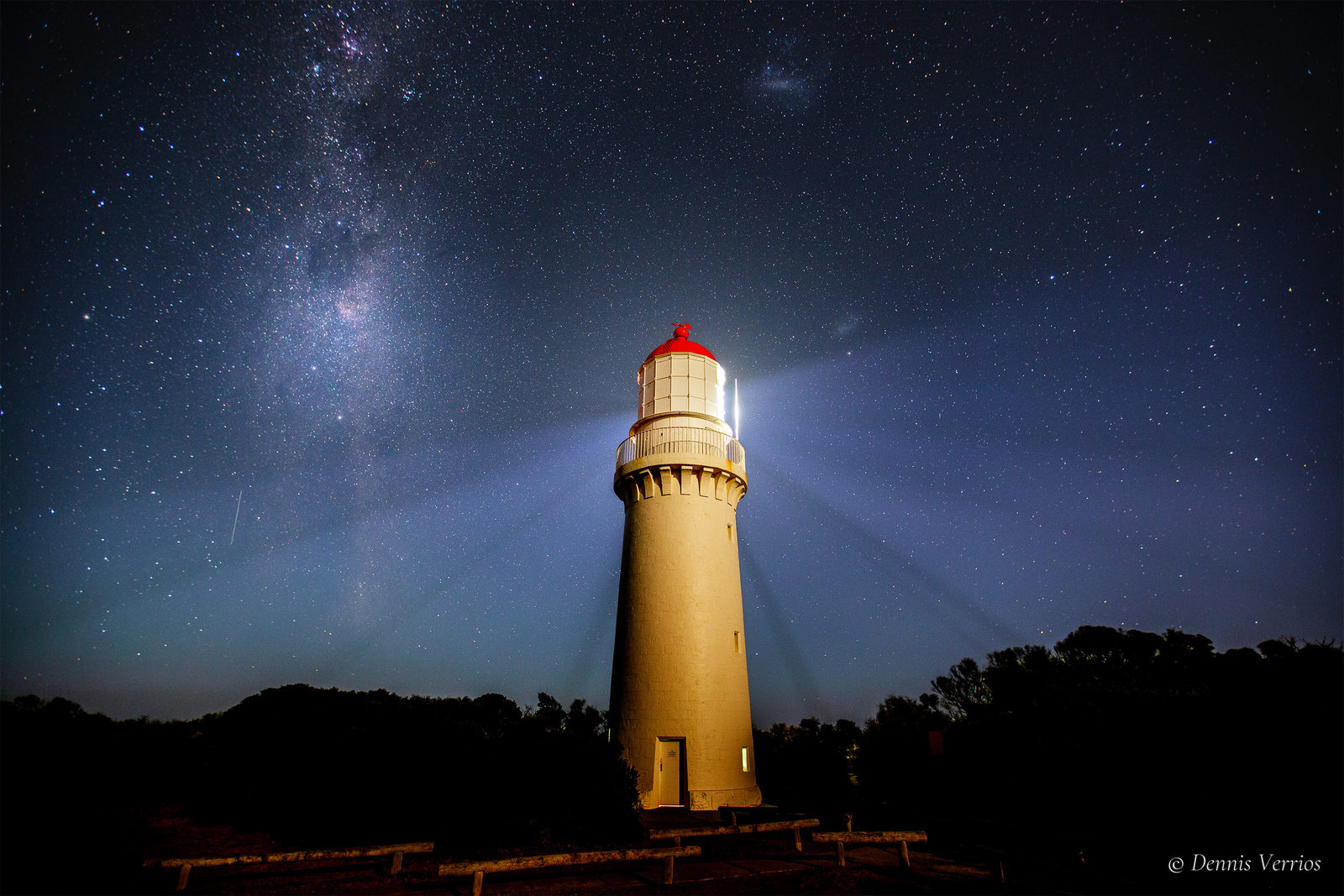 Cape Schanck Lighthouse on the Mornington Peninsula, its beams fanning out into a deep blue sky with the Milky Way rising on the left. Photograph by Dennis Verrios.