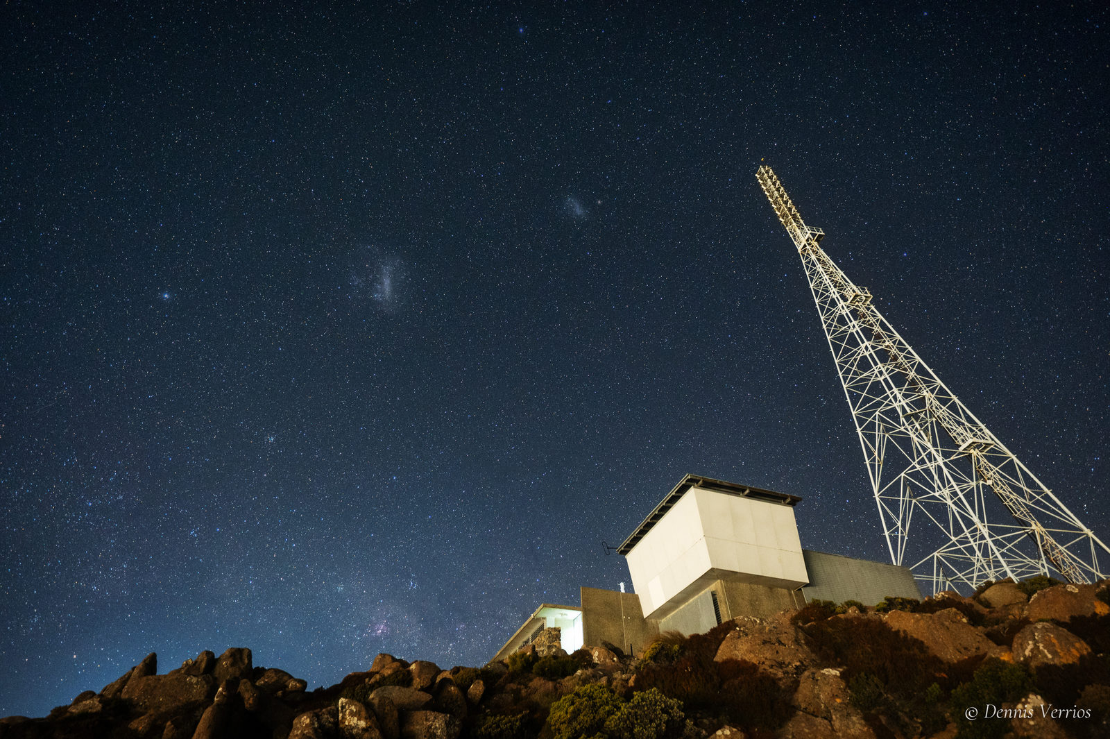 The Large and Small Magellanic Clouds in a star-filled sky above the transmitter mast, buildings and dolerite boulders on the summit of kunanyi / Mount Wellington, Tasmania. Photograph by Dennis Verrios.